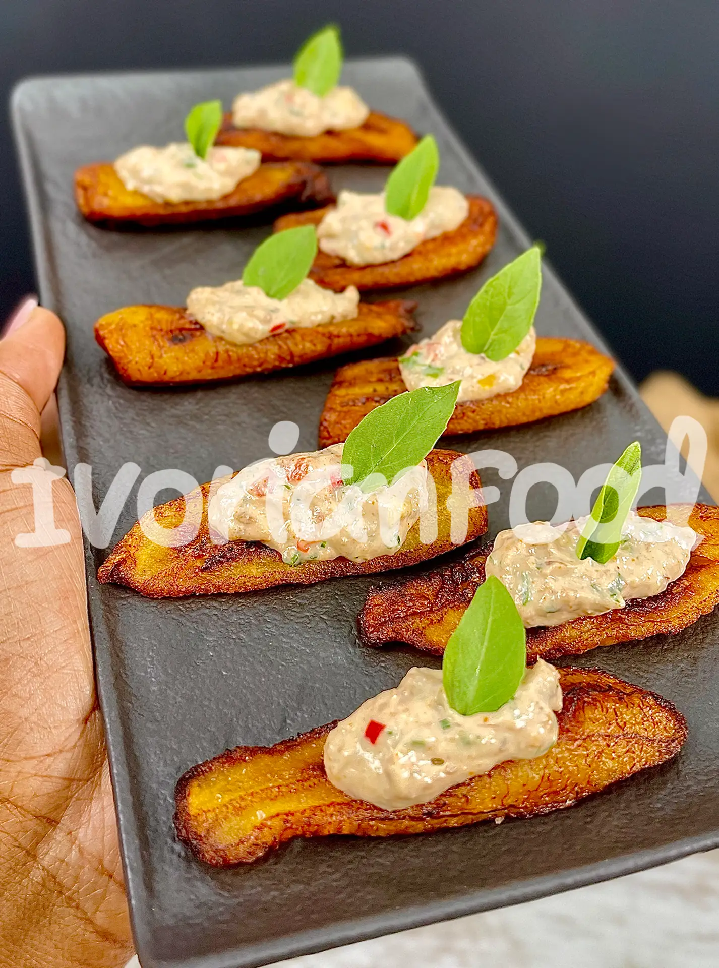 Bruschetta d'Alloco au Thon Crémeux est un mélange savoureux de banane plantain frite et d'une garniture onctueuse de thon à la crème, agrémentée de persil et ciboulette.